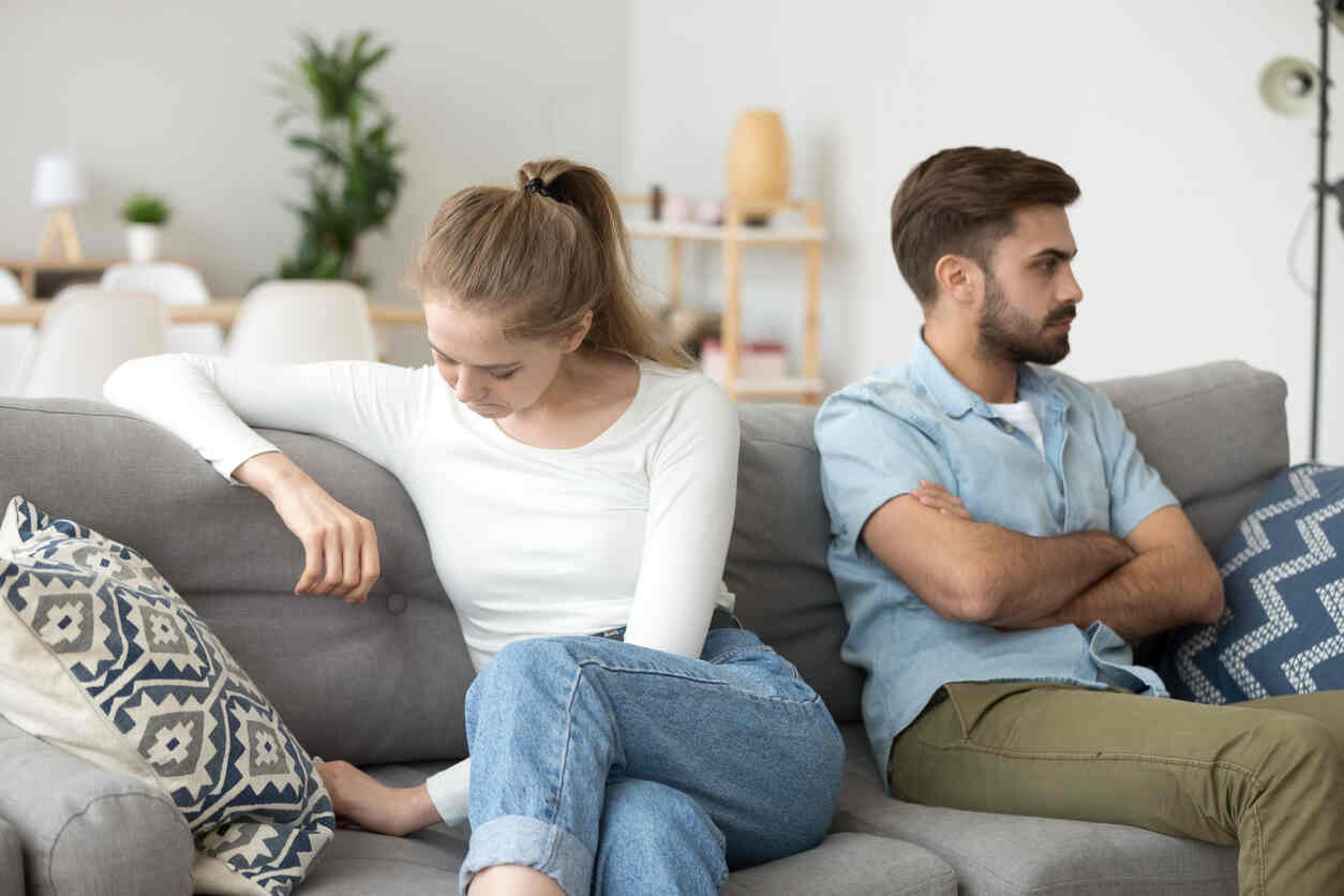 Couple sitting apart on a sofa, displaying signs of tension and emotional distress, representing a domestic dispute or conflict in a relationship.